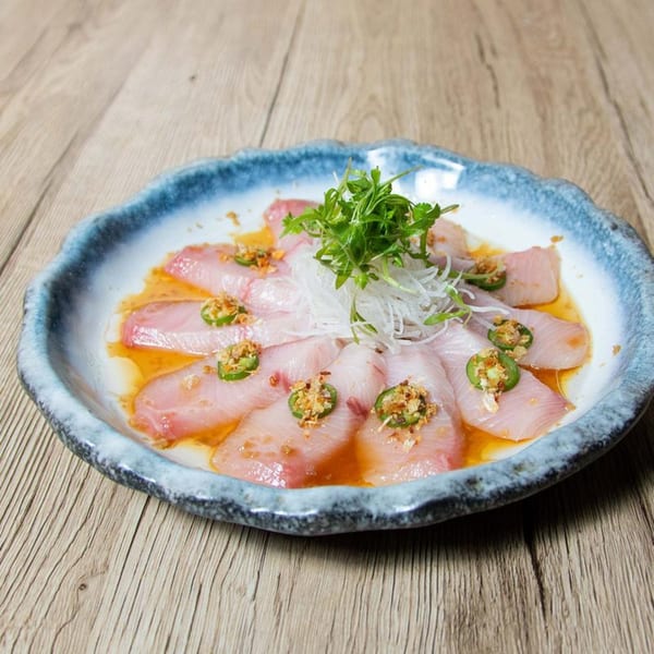 Soho Japanese Restaurant's yellowtail sashimi with jalapeño, garlic, and ponzu sauce in a blue-rimmed dish.