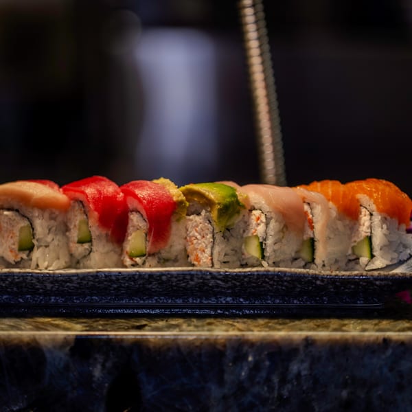 A row of colorful sushi rolls with various toppings on a dark, textured plate.