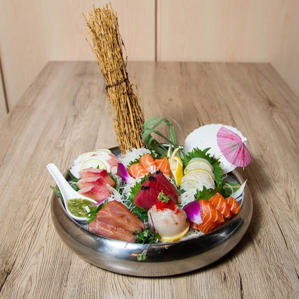 A large platter of assorted sashimi, including tuna, salmon, and scallops, garnished with lemon and a pink umbrella.
