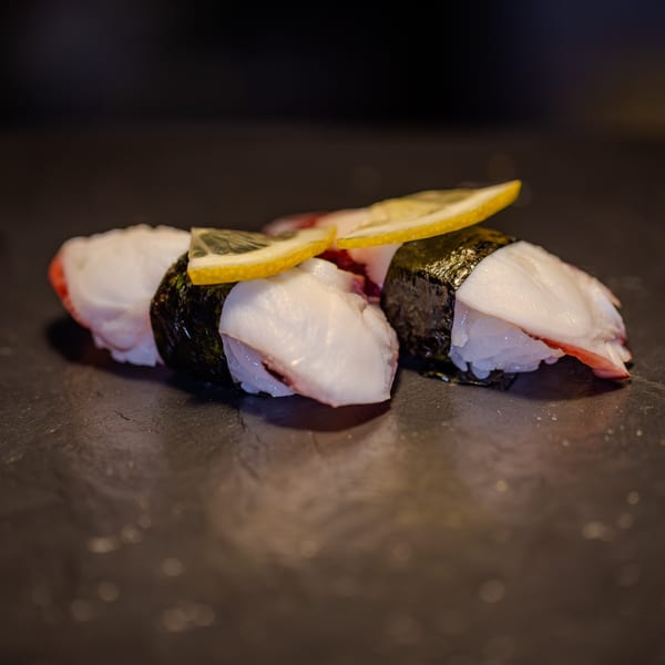 Three pieces of octopus nigiri sushi, garnished with lemon slices, on a dark surface.