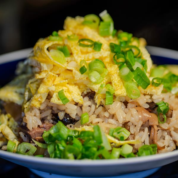 Close-up of Japanese fried rice with egg strips, mushrooms, and green onions in a white bowl.