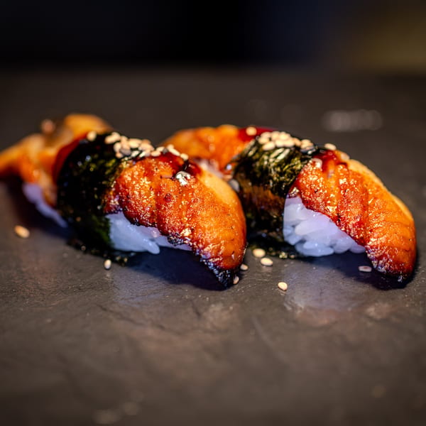 Two pieces of unagi nigiri sushi with dark eel, white rice, nori, and sesame seeds.