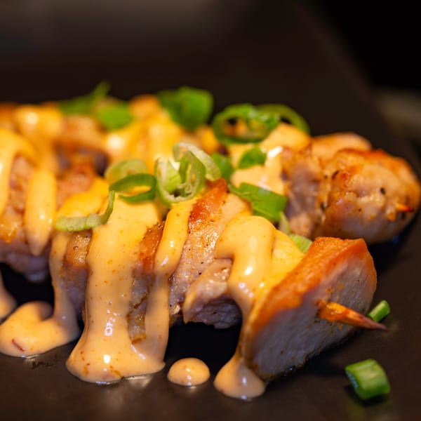 Chicken skewers with creamy orange sauce and green onions on a dark plate.