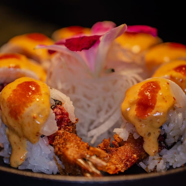 Soho Japanese Restaurant's sushi rolls with fried shrimp, sauce, and a pink flower garnish.