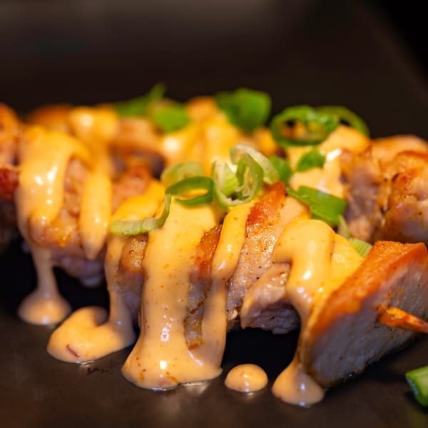 Close-up of Japanese yakitori skewers with creamy sauce and green onions on a dark plate.