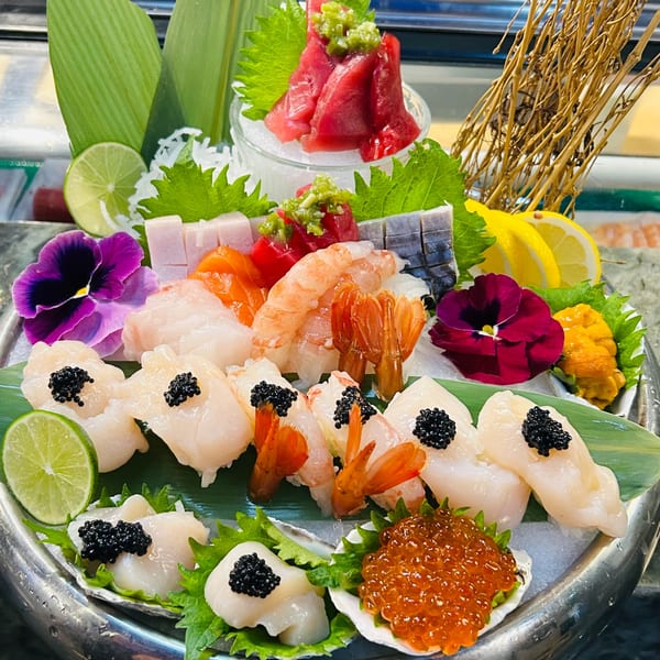 A large platter of assorted Japanese sushi and sashimi, garnished with flowers, limes, and lemons.
