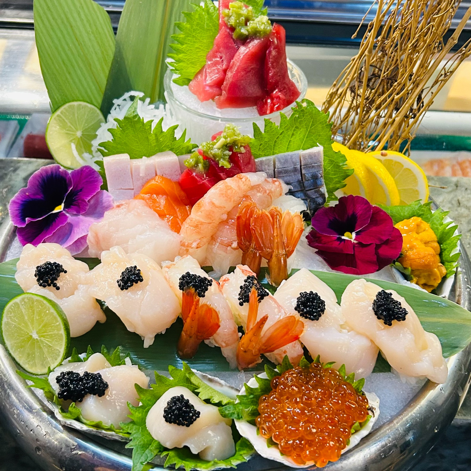 A large platter of assorted Japanese sushi and sashimi, garnished with flowers, limes, and lemons.