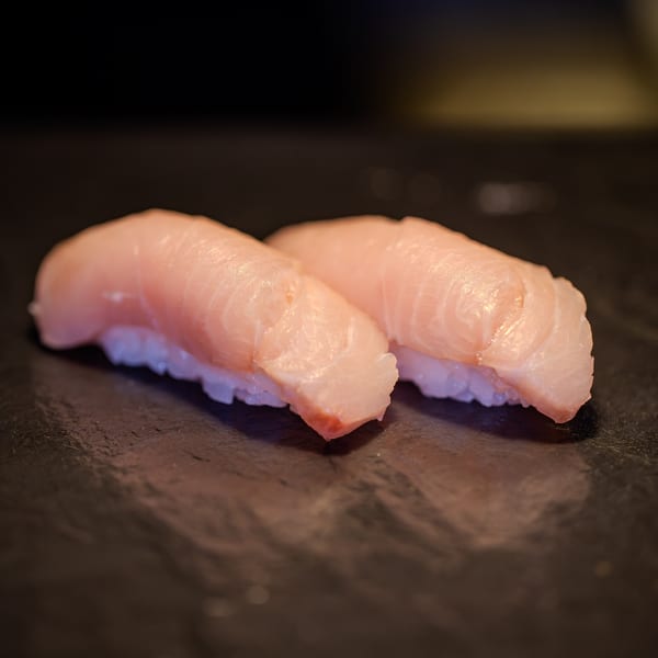 Two pieces of fresh yellowtail nigiri sushi with white rice on a dark surface.