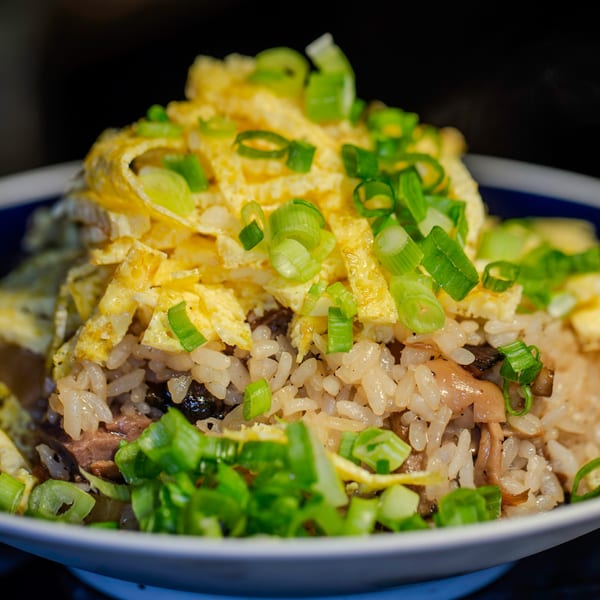 Japanese fried rice with scrambled egg strips and chopped green onions in a white bowl.