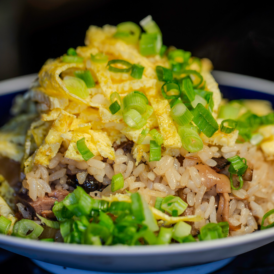 Japanese fried rice with scrambled egg strips and chopped green onions in a white bowl.