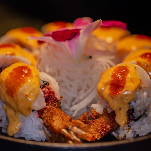 Close-up of Soho Japanese Restaurant's sushi rolls with fried shrimp, spicy sauce, and a pink flower garnish.