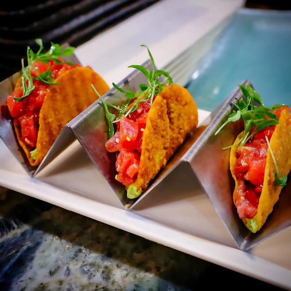 Three Japanese tacos with red tuna, avocado, and microgreens in crispy shells on a white plate.
