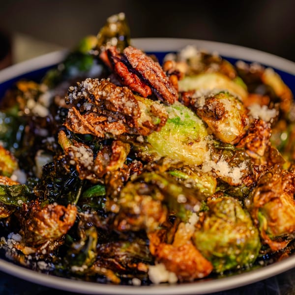 Close-up of crispy Brussels sprouts with pecans and grated cheese in a blue bowl.