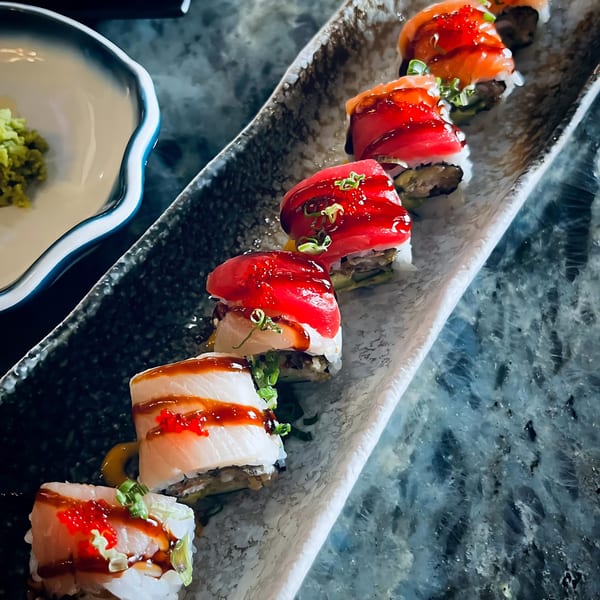 A long platter of colorful sushi rolls with various toppings, including tuna, salmon, and roe.