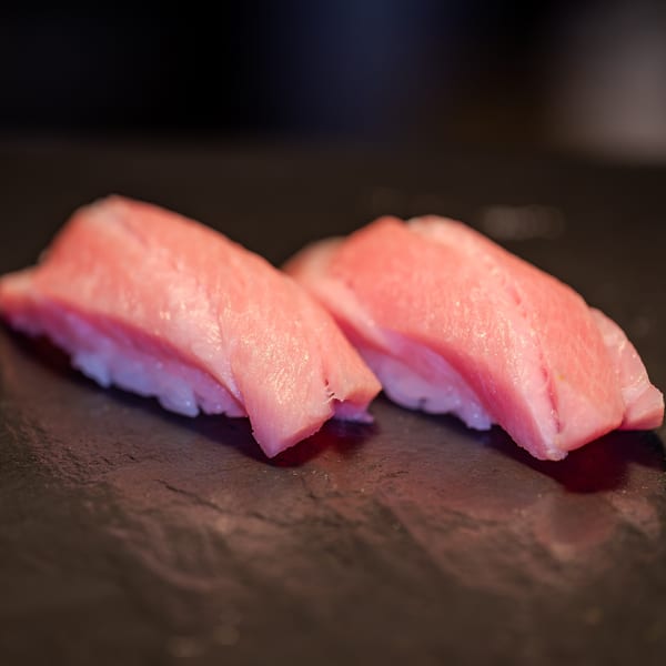Two pieces of pink tuna nigiri sushi with white rice on a dark surface.