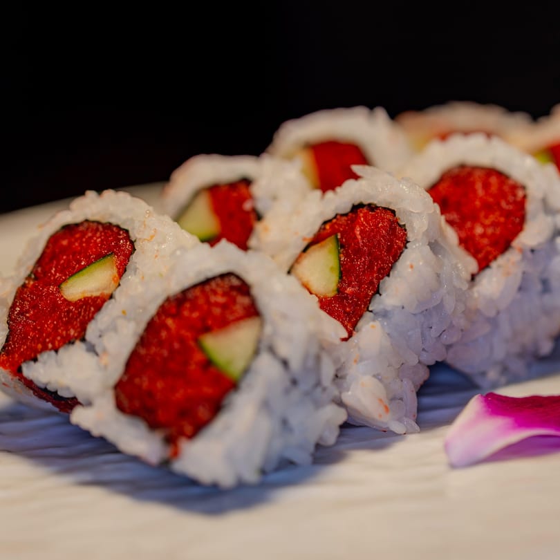 Close-up of Soho Japanese Restaurant's spicy tuna sushi rolls with cucumber and a pink orchid petal.