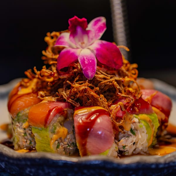 Soho Japanese Restaurant's sushi roll topped with crispy fried onions, sauces, and a pink orchid.