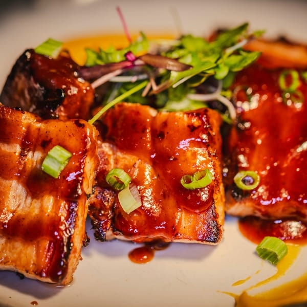 Glazed salmon pieces with green onions and a side salad on a white plate at Soho Japanese Restaurant.