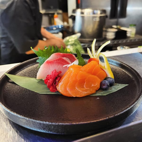 Platter of fresh salmon and tuna sashimi, garnished with lemon, blueberries, and a red flower.