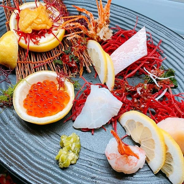 A Japanese seafood platter with uni, ikura, shrimp, scallops, and white fish sashimi, garnished with lemon.